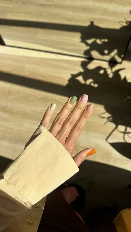 Short nails in white, sage, pink and nude with a tangerine thumb, in afternoon sun