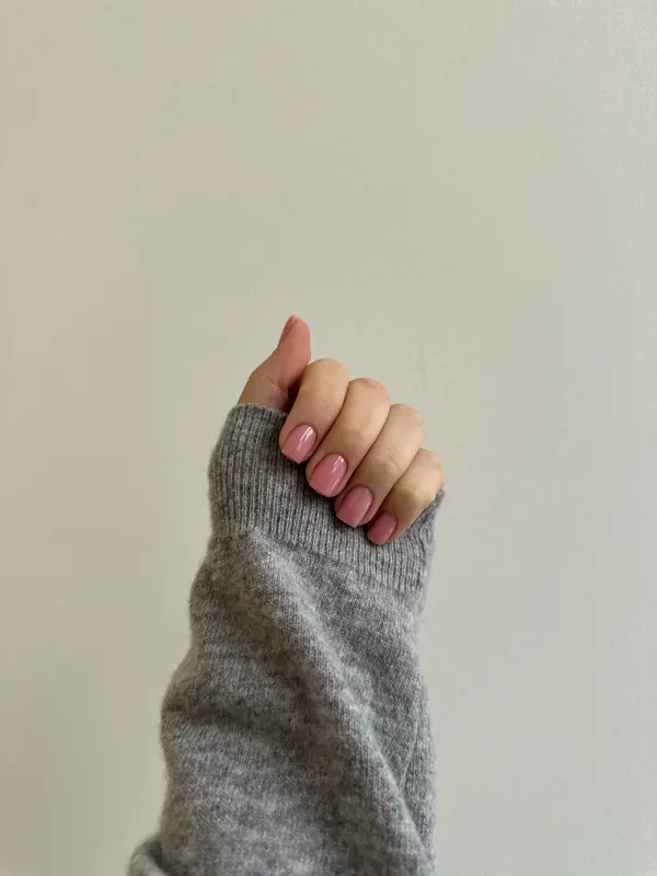 Short nails in a soft bubblegum pink against a grey knit sleeve